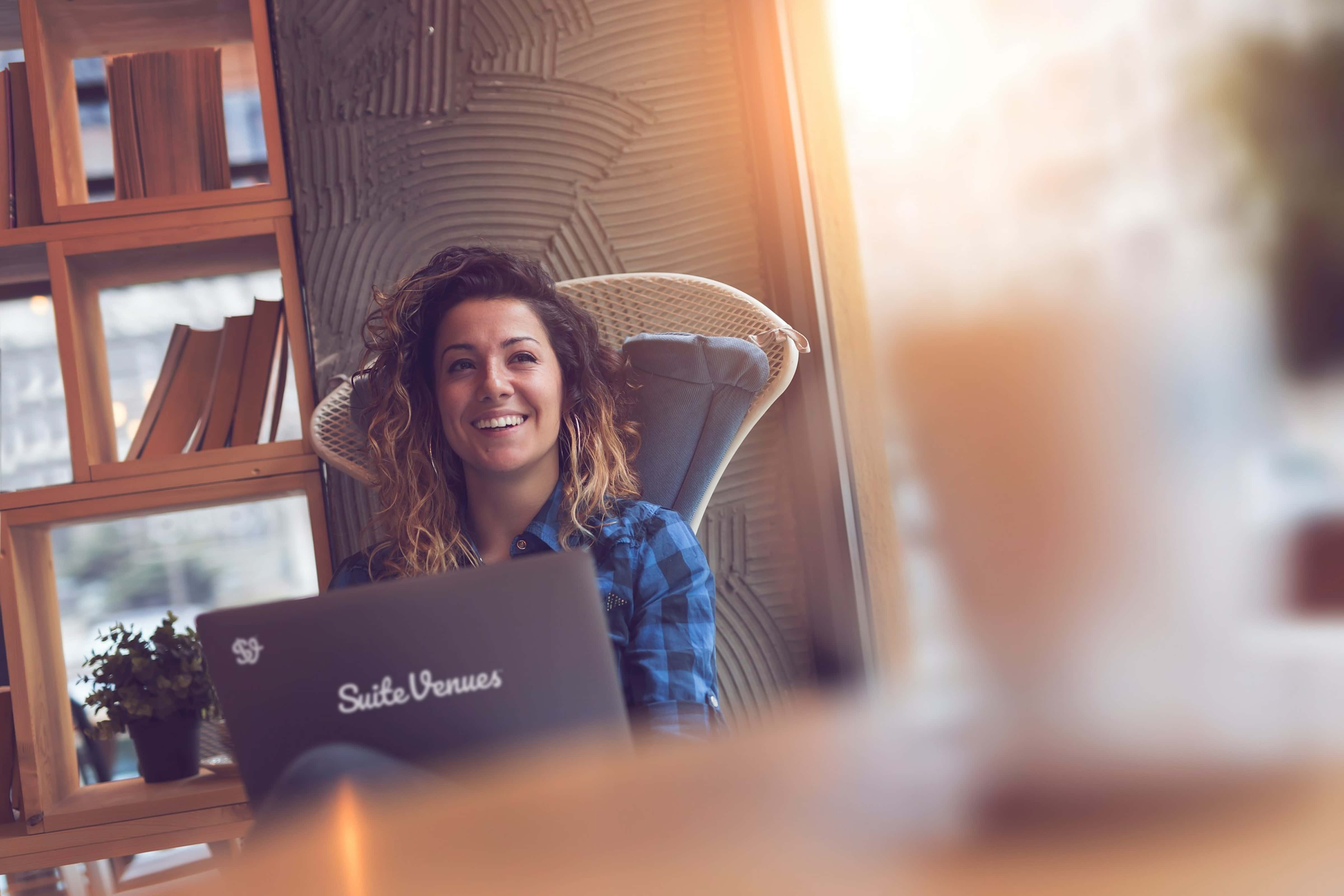 A smiling SuiteVenues team member sitting behind a laptop in a cozy, sunlit café